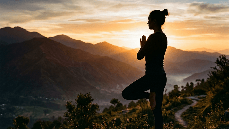 Person doing yoga at sunrise with mountains in the background